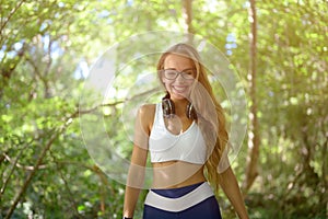 happy laughing pretty young girl in sportswear and glasses with wireless headphones in green park during summer sport