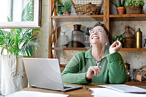 Happy laughing senior woman in front of laptop monitor. She sitting in home interior and having online conversation with