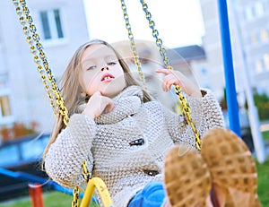 Happy laughing teen girl with long hair wearing a knitted cardigan enjoying a swing ride on a sunny autumn playground in