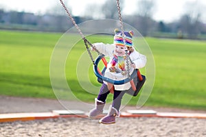 Happy laughing toddler girl swinging on playground