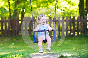 Happy laughing toddler girl swinging ride on playground