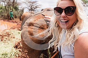 Happy laughing woman gets a photo taken as she pets a baby elephant