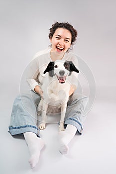 Happy laughing woman and her dog looking at camera sitting on grey floor.