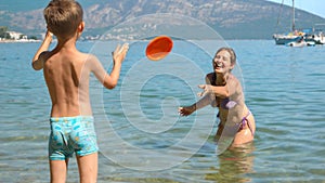 Happy laughing woman playing frisbee with her son on sunny sea beach during summer holidays