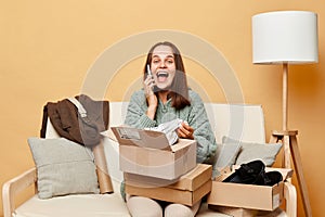 happy laughing woman sitting on sofa among boxes with clothing talking on mobile phone being in good mood boasting her online