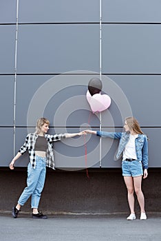 Happy lesbian couple holding hands with air balloons outdoors