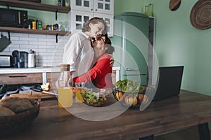 Happy lesbian couple hugging while standing in the kitchen at home. Cooking together, healthy eating