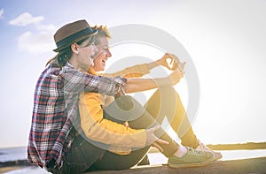 Happy lesbian couple taking a selfie with mobile smart phone camera on the beach at sunset - Vignette edit