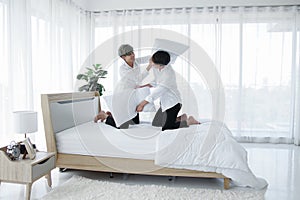 Happy LGBT Asian gay couple smiling playing pillow fight on bed at home. Young man smiling hitting his boyfriend with pillows