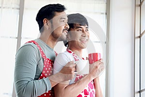 Happy LGBT couple has romantic moment together on Valentine Day. Asian gay males love hug and drink coffee beverage from mug while