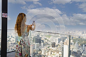 Happy lifestyle tourist woman take a picture by Photo camera of a smartphone with evening  scene in the cityscape on the rooftop