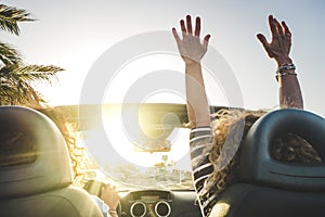 Happy lifestyle women couple enjoy travel with convertible car dancing and driving in the sunset - concept of joyful leisure