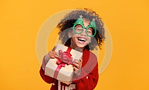 Happy little african american boy wearing funny glasses in form of Christmas trees with xmas gift