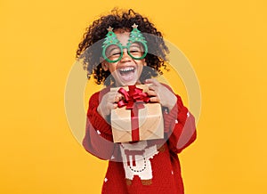 Happy little african american boy wearing funny glasses in form of Christmas trees with xmas gift