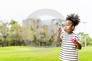 Happy little african american curly hair girl blowing soap bubbles playing alone in the park, Black hair style