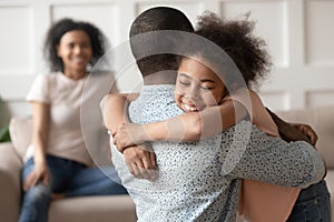 Happy little african kid daughter embracing black dad at home