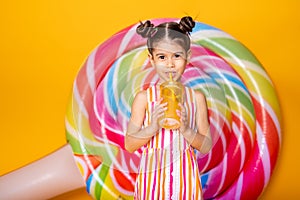 Happy little arab child girl in colorful striped dress drinking orange juice on yellow background