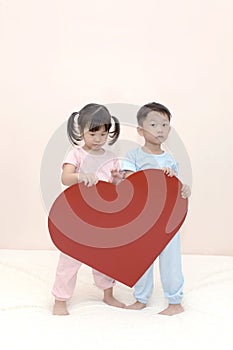 Happy little Asian boy and girl with a red heart over pink background.