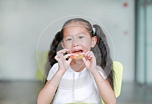 Happy little Asian child girl eating a piece of sliced tomato. Kid eating healthy food concept