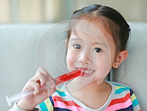 Happy little Asian child girl feeding liquid medicine with a syringe by self