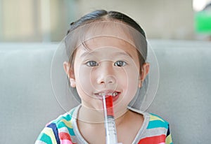 Happy little Asian child girl feeding liquid medicine with a syringe by self