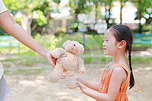 Happy little Asian child girl get a teddy bear doll from her mother in the park outdoor. Surprise gift from mom for daughter