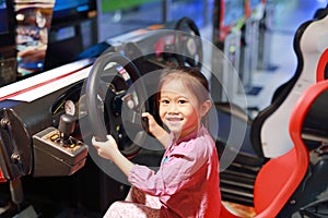 Happy little Asian child girl playing arcade video game. Racing car