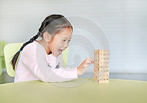 Happy little Asian child girl playing wood blocks tower game for Brain and Physical development skill in a classroom. Focus at