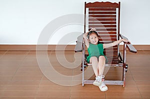 Happy little Asian child girl relaxing on Thai wooden traditional chair