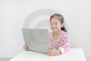 Happy little asian child girl sitting at desk and using laptop computer stay at home