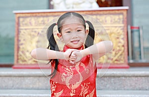 Happy little Asian child girl wearing red cheongsam with greeting gesture celebration for Chinese New Year at chinese temple in