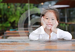 Happy little Asian kid girl lying on the wooden table with looking camera