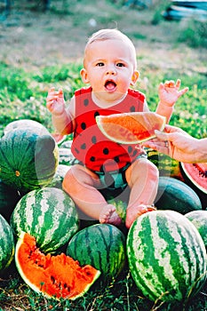 Happy little baby boy in funny costume sitting and eating slice of watermelon