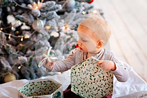 Happy little baby boy opening present boxes near Christmas tree