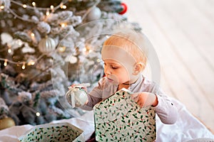 Happy little baby boy opening present boxes near Christmas tree