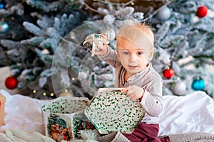 Happy little baby boy opening present boxes near Christmas tree