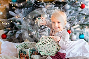 Happy little baby boy opening present boxes near Christmas tree