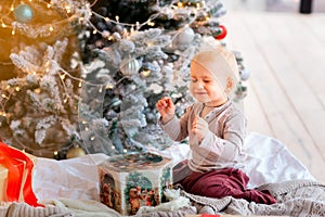Happy little baby boy opening present boxes near Christmas tree