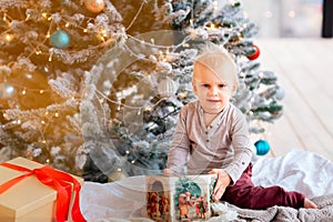 Happy little baby boy opening present boxes near Christmas tree