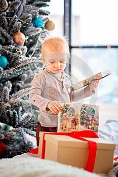 Happy little baby boy opening present boxes near Christmas tree
