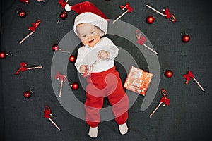 Happy little baby boy in Santa Claus hat smiling among Christmas candy canes