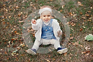 Happy little baby boy sitting on the grass in the park, garden, meadow. Baby looks at parents, beautiful warm weather