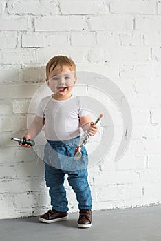 happy little baby boy with toys standing at white