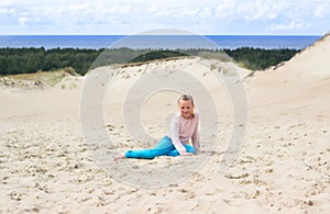 Happy little baby girl enjoys sand playing in the dunes