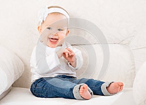 Happy little baby girl laughing and sitting on a sofa in jeans