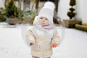 Happy little baby girl making first steps outdoors in winter through snow. Cute toddler learning walking. Child having