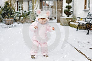 Happy little baby girl making first steps outdoors in winter through snow. Cute toddler learning walking. Child having