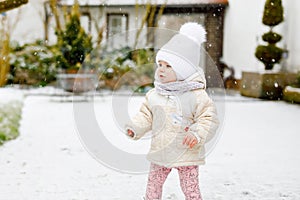 Happy little baby girl making first steps outdoors in winter through snow. Cute toddler learning walking. Child having