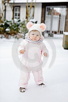 Happy little baby girl making first steps outdoors in winter through snow. Cute toddler learning walking. Child having