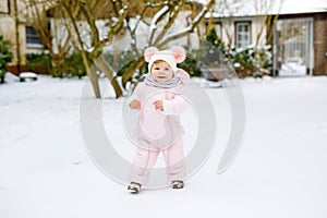 Happy little baby girl making first steps outdoors in winter through snow. Cute toddler learning walking. Child having